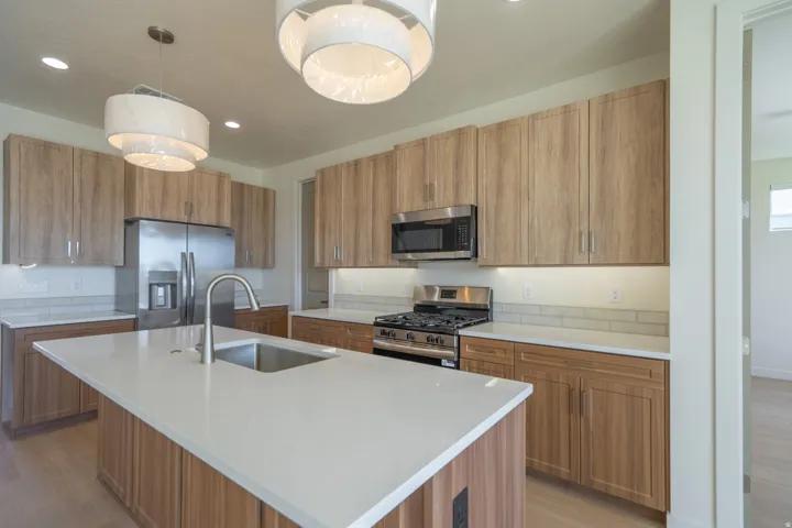 Kitchen featuring a central island with an undermount sink, light wood-finish cabinetry, stainless steel appliances, white countertops, and subway tile backsplash