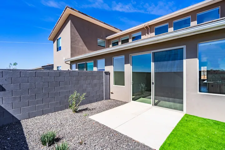 Outdoor patio featuring a sliding glass door, a section of green turf, a gravel area with desert landscaping, and a block wall
