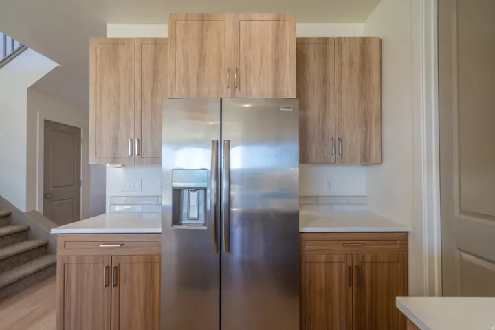 Kitchen area featuring wood-finish cabinetry, stainless steel refrigerator, white countertops, and subway tile backsplash