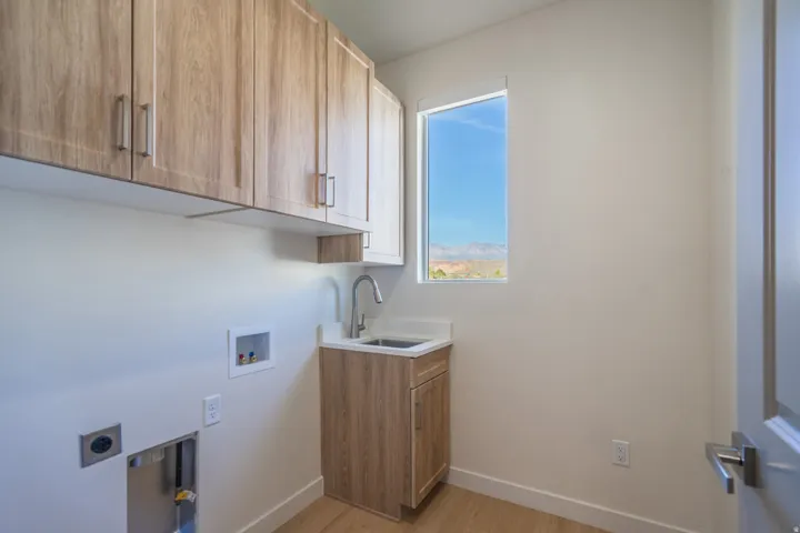 Dedicated utility area featuring wood-finish upper cabinetry, a utility sink with a high-arc faucet, and wood-finish flooring