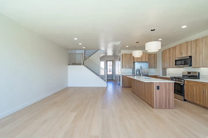 Open-concept living space featuring wood-finish flooring, a modern kitchen with a large island, stainless steel appliances, and wood cabinetry