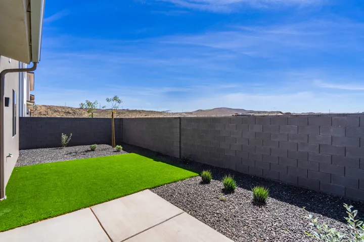 Private backyard featuring a concrete patio, artificial turf, and dark gravel landscaping with low-maintenance plantings