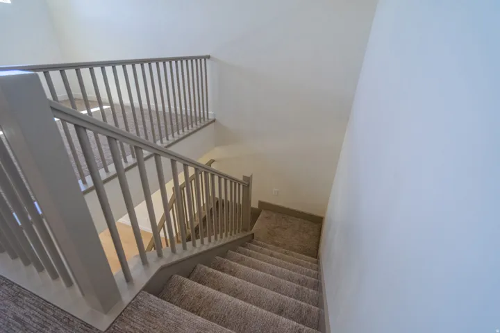 Multi-level staircase featuring light gray painted balusters and handrails, complemented by neutral-toned carpeting on both the stairs and the upper landing