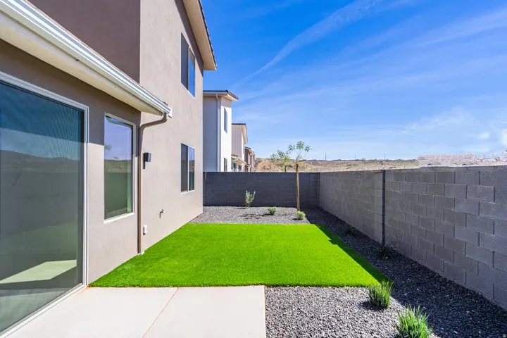 Private backyard featuring artificial turf, gravel landscaping, a concrete patio, and a block wall perimeter