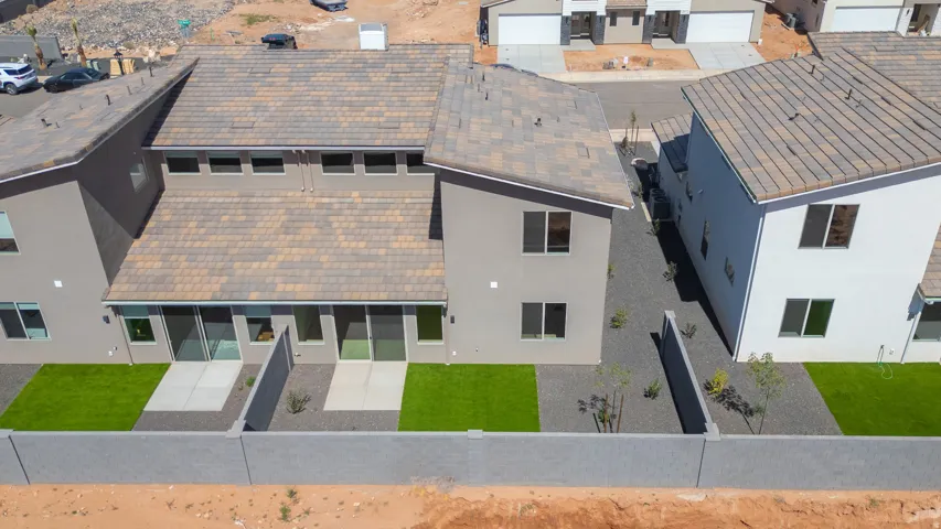 Rear exterior featuring a concrete block perimeter wall, a combination of artificial turf and gravel landscaping, two concrete patios, and multiple sliding glass doors