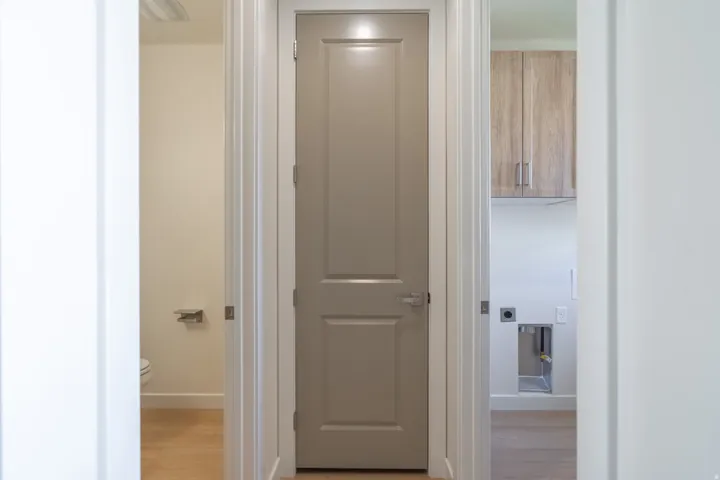 Hallway featuring light wood-finish flooring, white trim, and a gray panel door