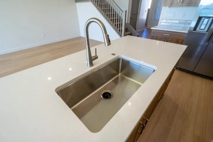 Modern kitchen island featuring a sleek undermount stainless steel sink with a contemporary pull-down faucet, white quartz countertop, and wood-finish cabinetry