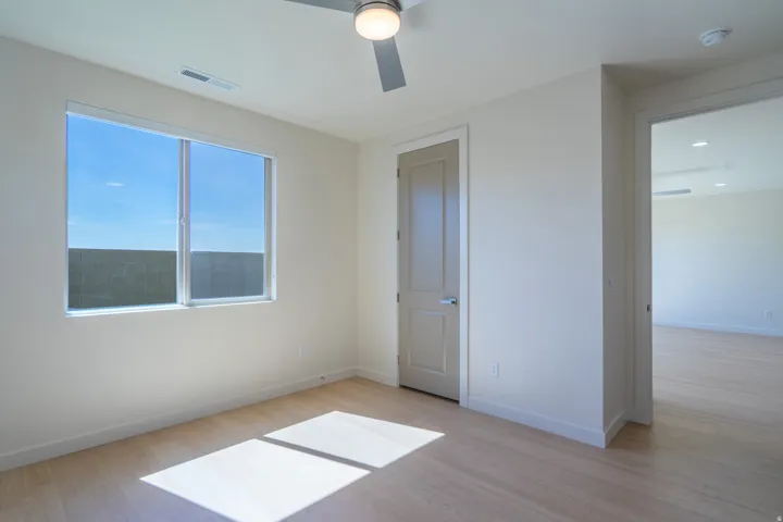 Spacious room featuring light wood-finish flooring, a large window, a ceiling fan with integrated lighting, and a neutral color palette