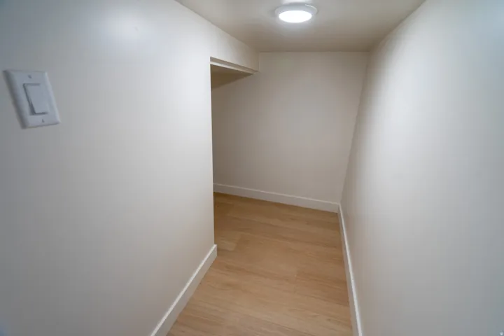 Compact storage area featuring wood-finish flooring, white baseboards, a recessed ceiling light, and a wall-mounted light switch