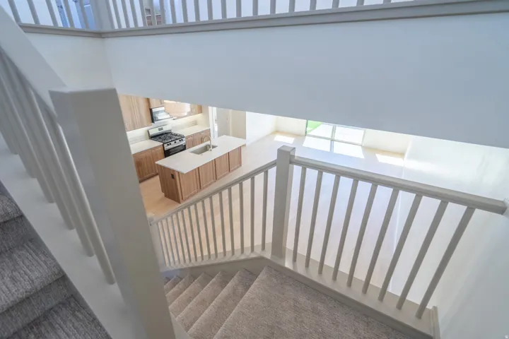 Carpeted staircase with white balusters overlooking an open-concept living space