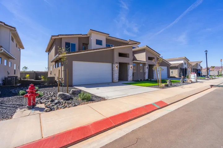Contemporary multi-level exterior featuring a two-car garage, stone accents, and a low-maintenance landscape with artificial turf