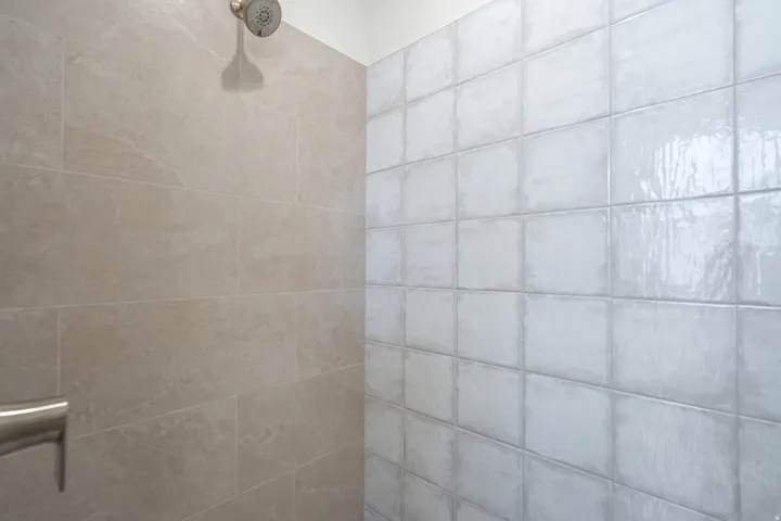 Shower enclosure featuring two-toned tilework and a brushed nickel showerhead