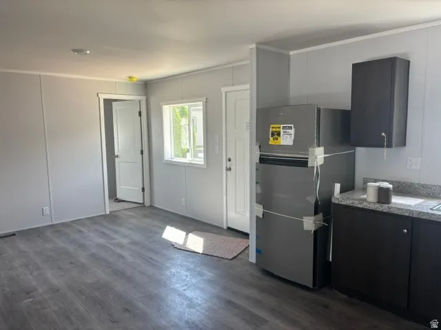 Open-concept living area featuring wood-finish flooring, a contemporary refrigerator, dark cabinetry, and speckled countertops