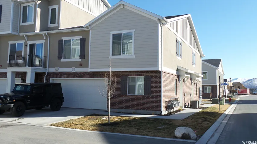 Modern two-story home featuring a brick and siding exterior, two-car garage with white overhead door, and a manicured front lawn with young landscaping