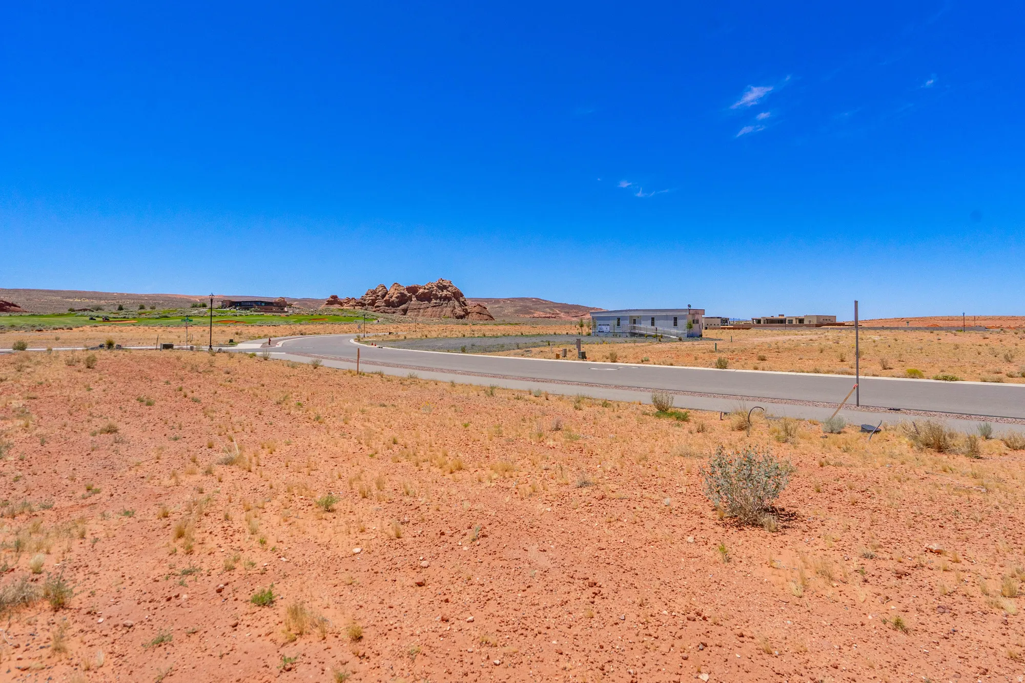 Expansive undeveloped land featuring a paved road, natural desert landscaping, and distant rock formations