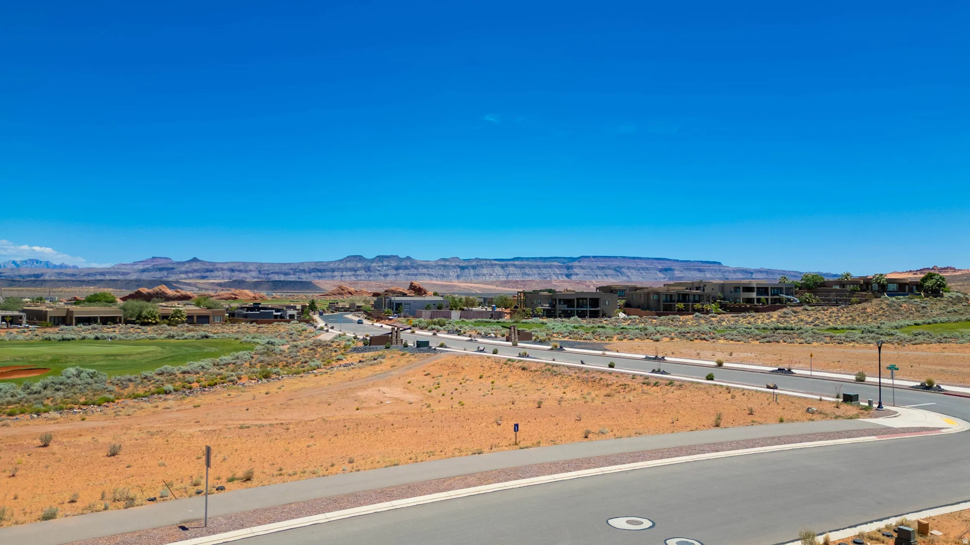 Expansive desert landscape featuring a paved street and distant golf course