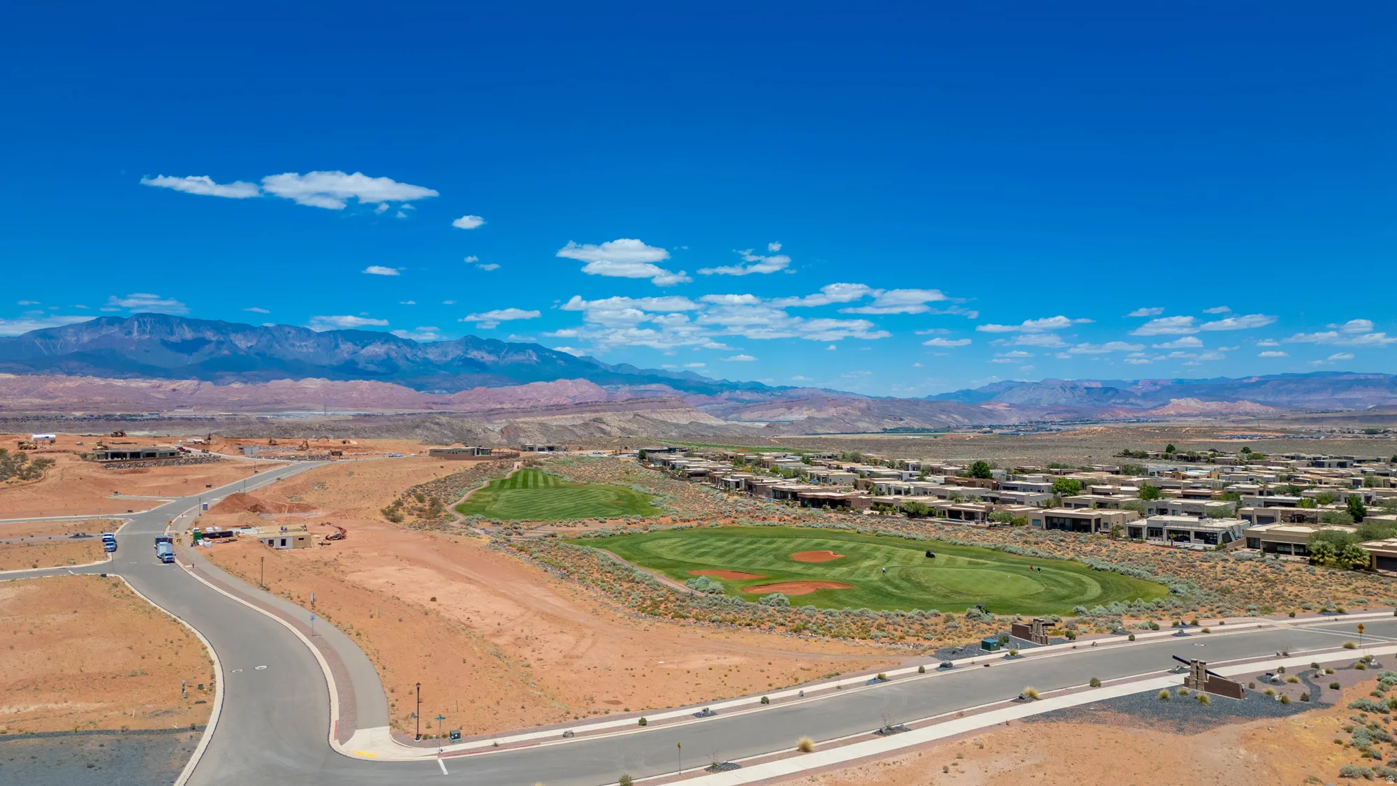 Expansive desert landscape featuring a golf course, residential structures, paved roads, and distant mountains under a clear sky
