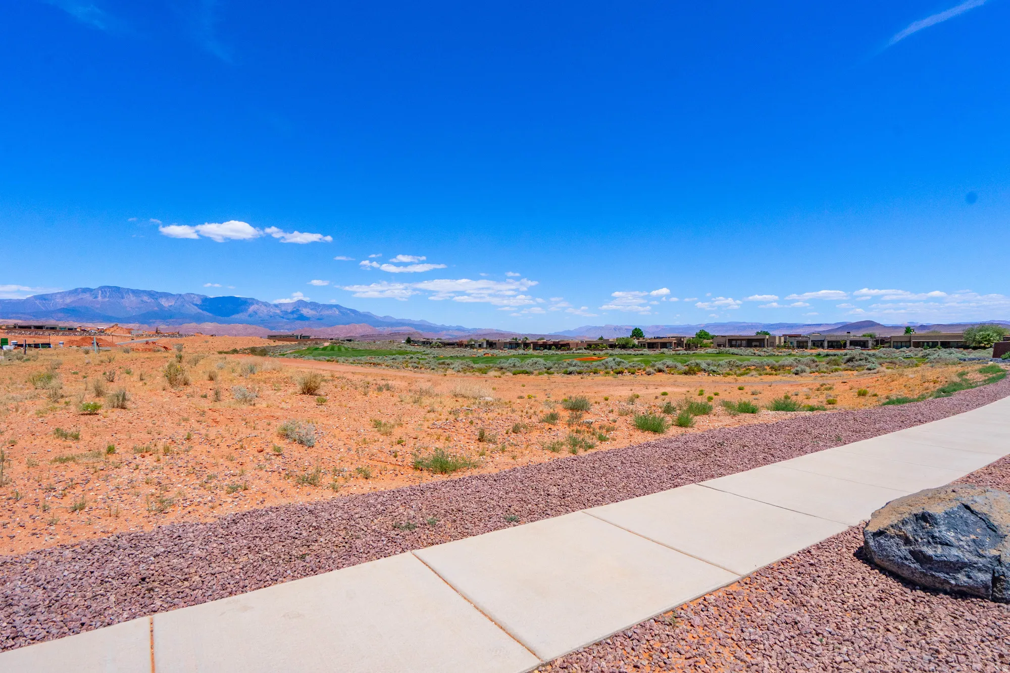Expansive vacant lot featuring clean concrete walkways, decorative rock landscaping, and mature vegetation