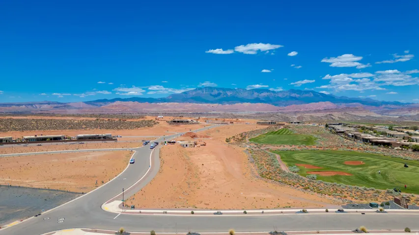 Expansive desert landscape with a paved road, scattered modern homes, and a manicured golf course