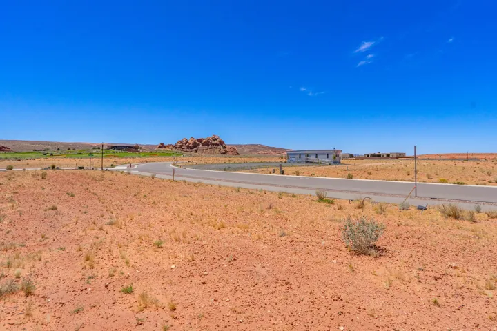 Expansive undeveloped land featuring a paved road, natural desert landscaping, and distant rock formations