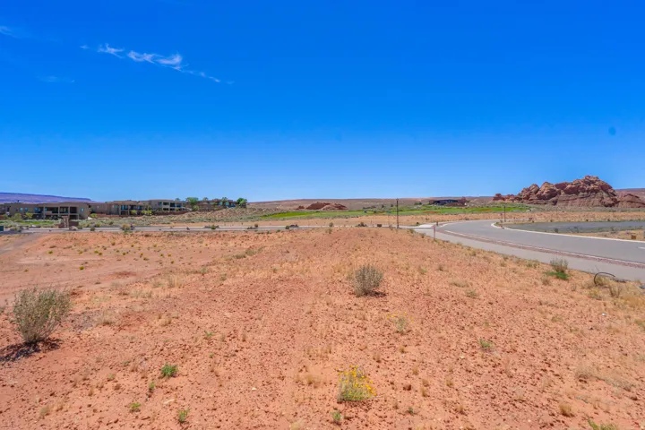 Expansive desert lot featuring red clay soil, sparse native vegetation, and direct road frontage