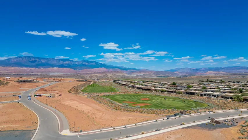 Expansive desert landscape featuring a golf course, residential structures, paved roads, and distant mountains under a clear sky
