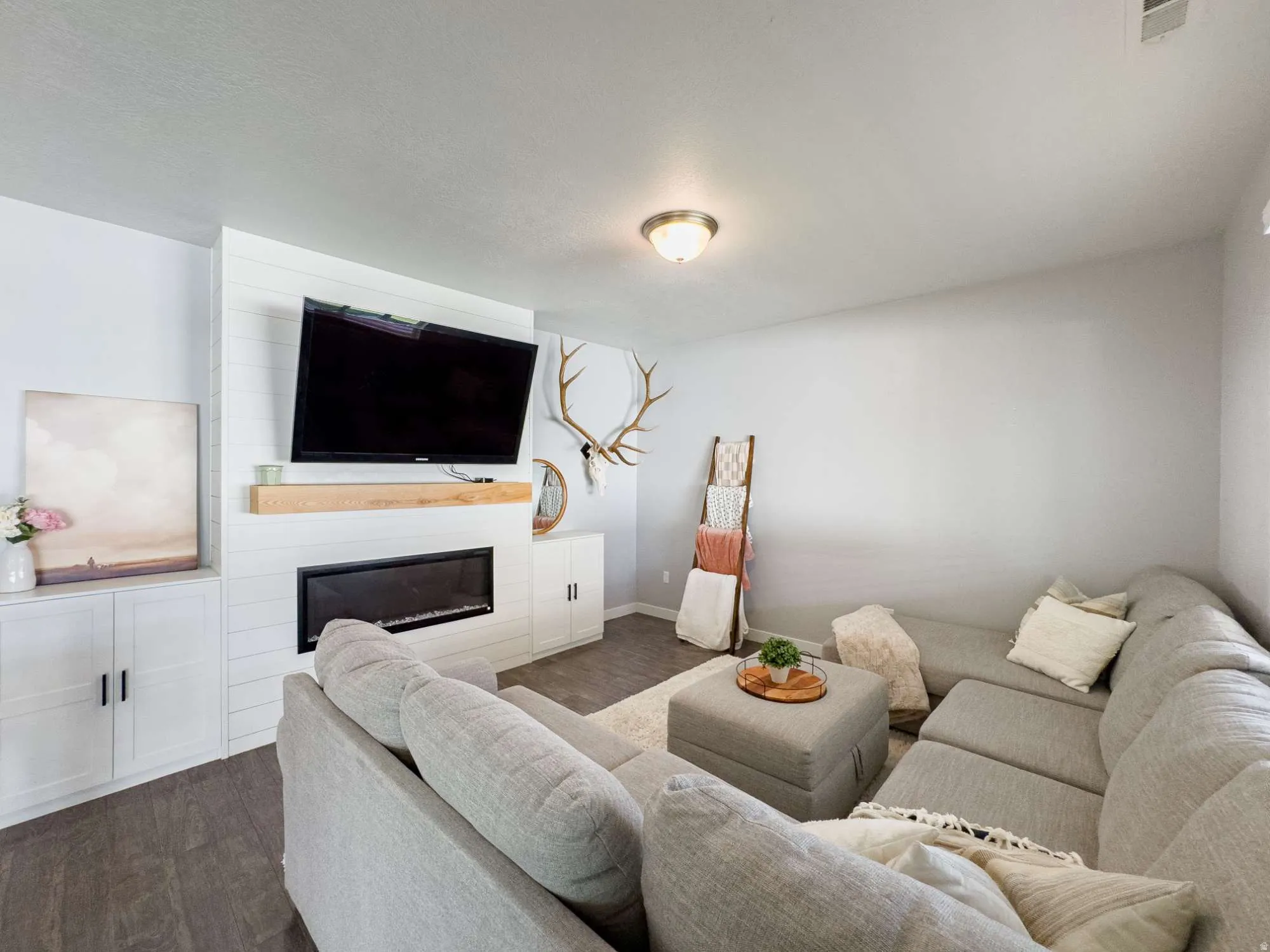 Living area featuring a modern linear fireplace with a wood mantel, shiplap wall accent, and built-in cabinetry