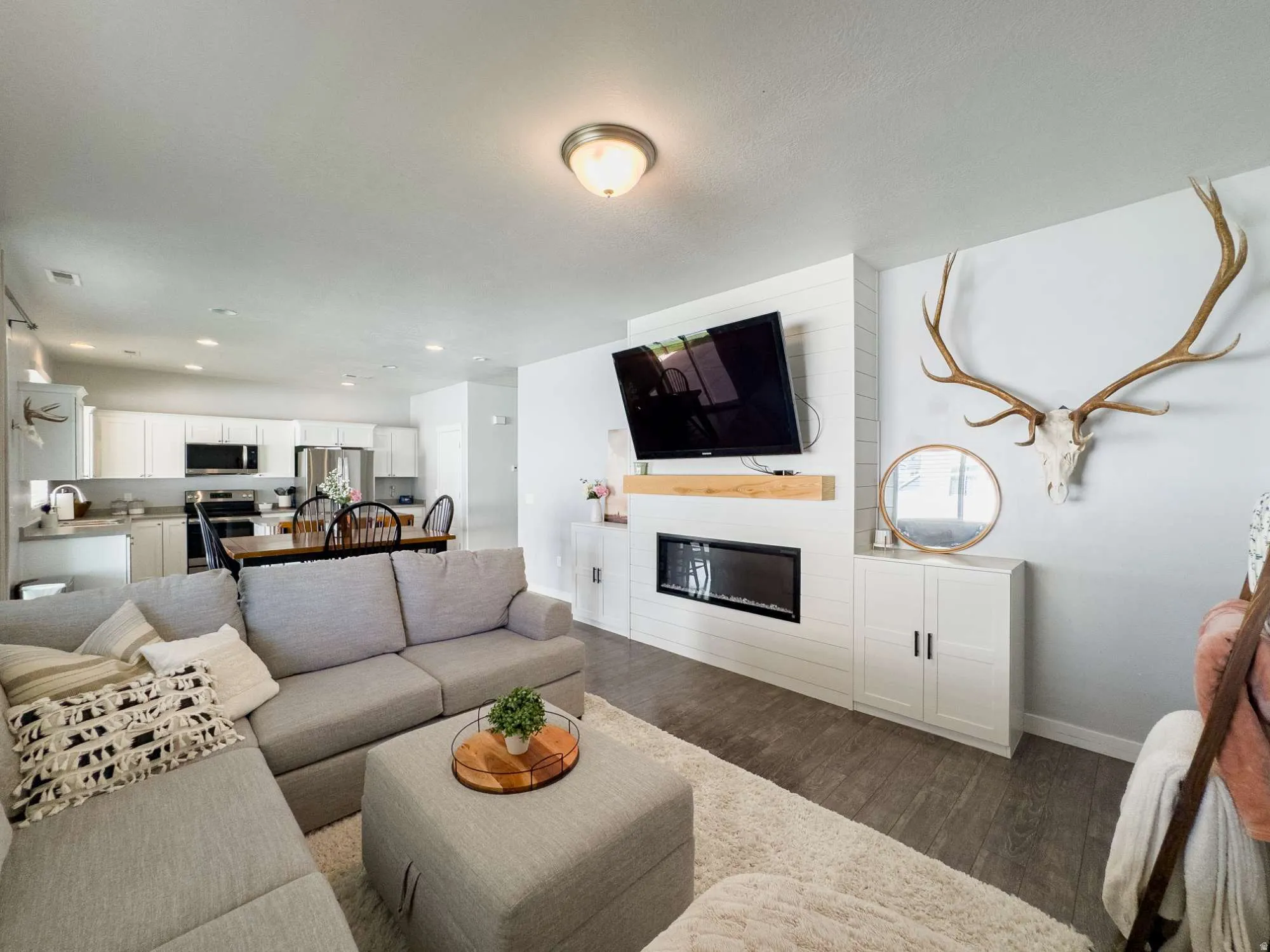 Living area featuring wood-finish flooring, a contemporary electric fireplace with a wood mantle, custom built-in cabinetry, and recessed lighting