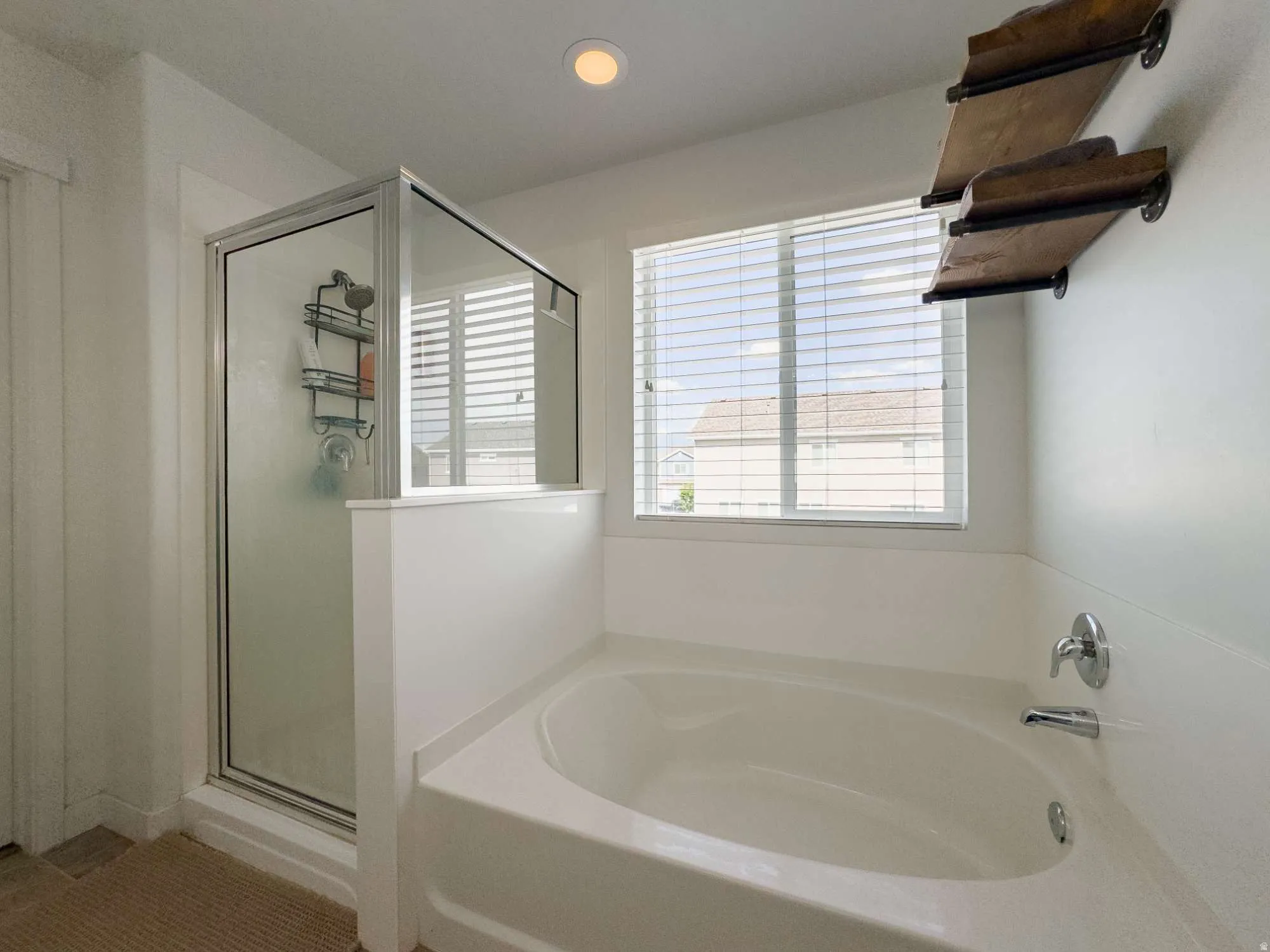 Soaking tub with brushed chrome fixtures, a clear glass shower enclosure, and a window with horizontal blinds