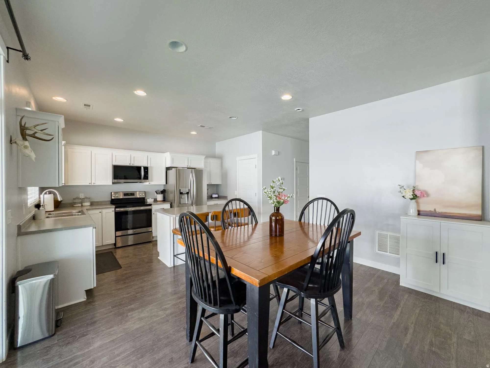 Open-concept dining and kitchen area featuring a wood-finish dining table with seating for six, stainless steel appliances, white cabinetry with hardware accents