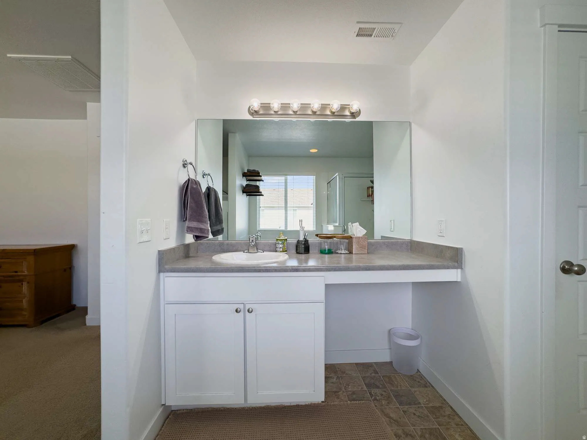 Bright and functional master bathroom featuring a large frameless mirror, white cabinetry with ample storage, a ceramic vessel sink, and white cabinets