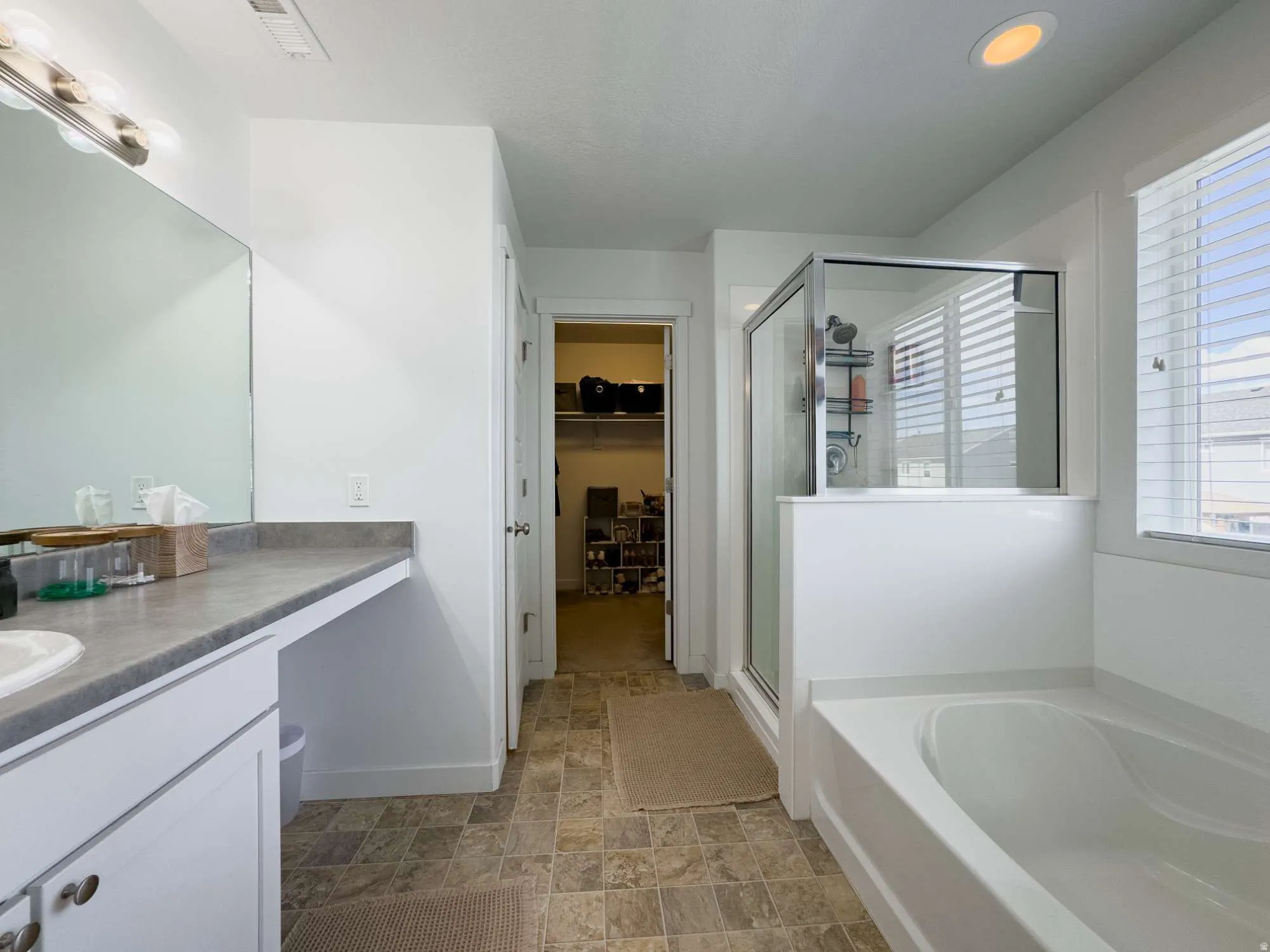 Bathroom featuring a built-in bathtub, a walk-in shower with a glass enclosure, a vanity with a white basin sink and a stone-finish countertop, and tiled flooring and walk in closet.