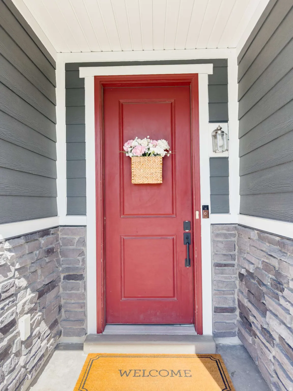 Welcoming entry featuring a striking red six-panel door with polished hardware, framed by white trim and flanked by stacked stone veneer siding
