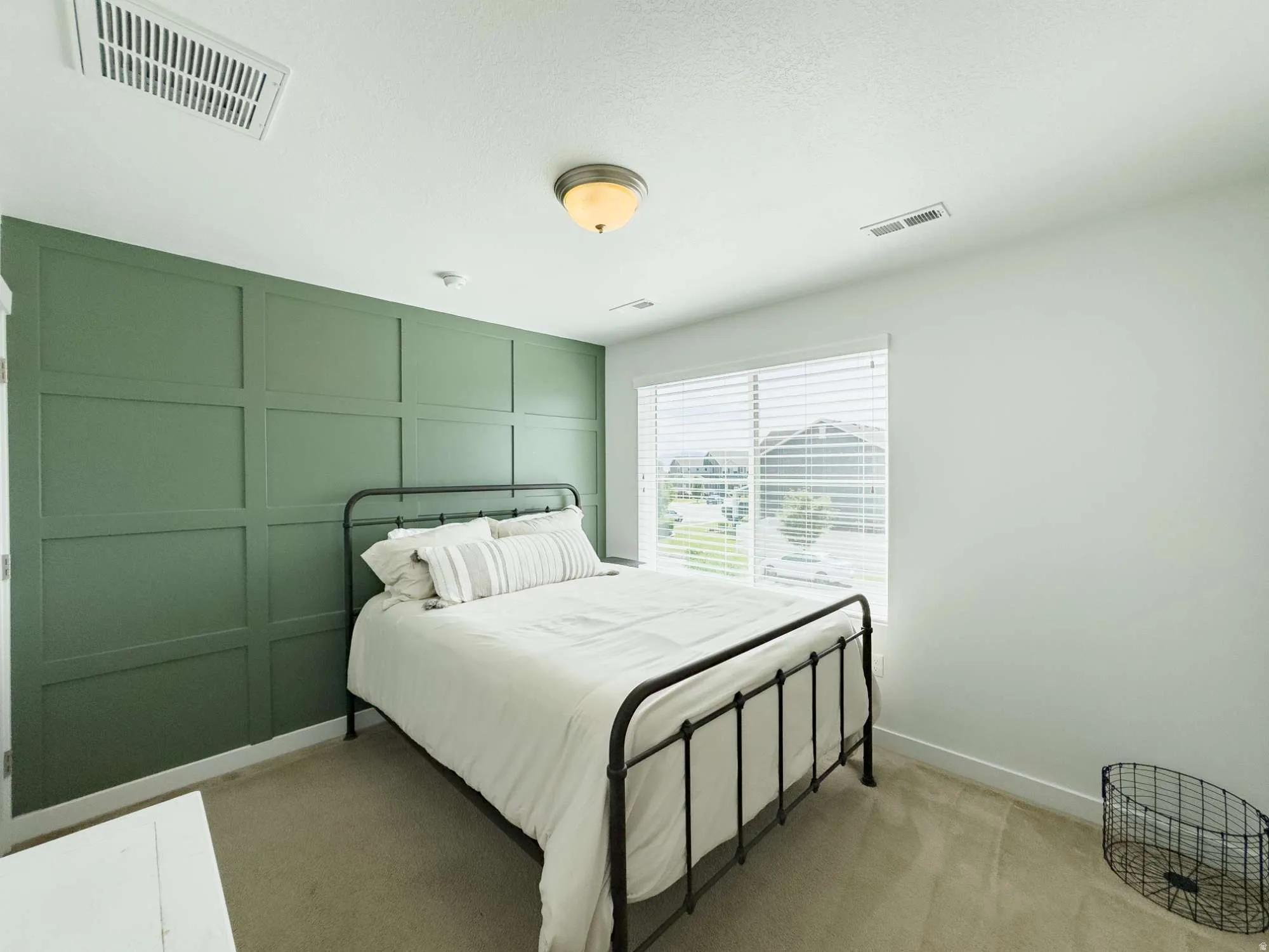 Bedroom featuring a statement sage green paneled accent wall, metal bed frame with white bedding, large sliding glass doors with plantation shutters, neutral flooring, and recessed ceiling lighting