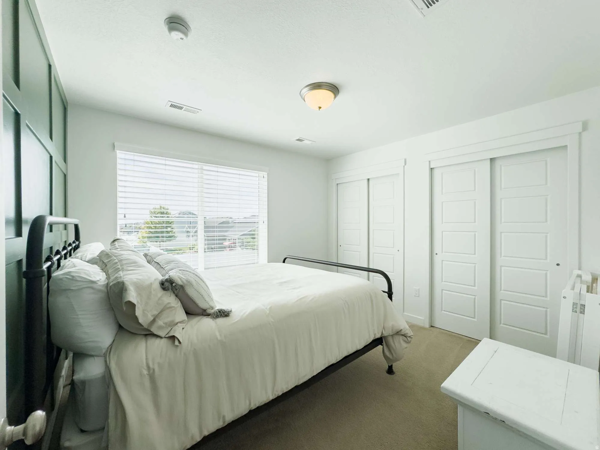 Light-filled interior featuring a large window with horizontal blinds, a ceiling-mounted light fixture, two sliding closet doors with panel detailing, and a feature wall with vertical and horizontal trim