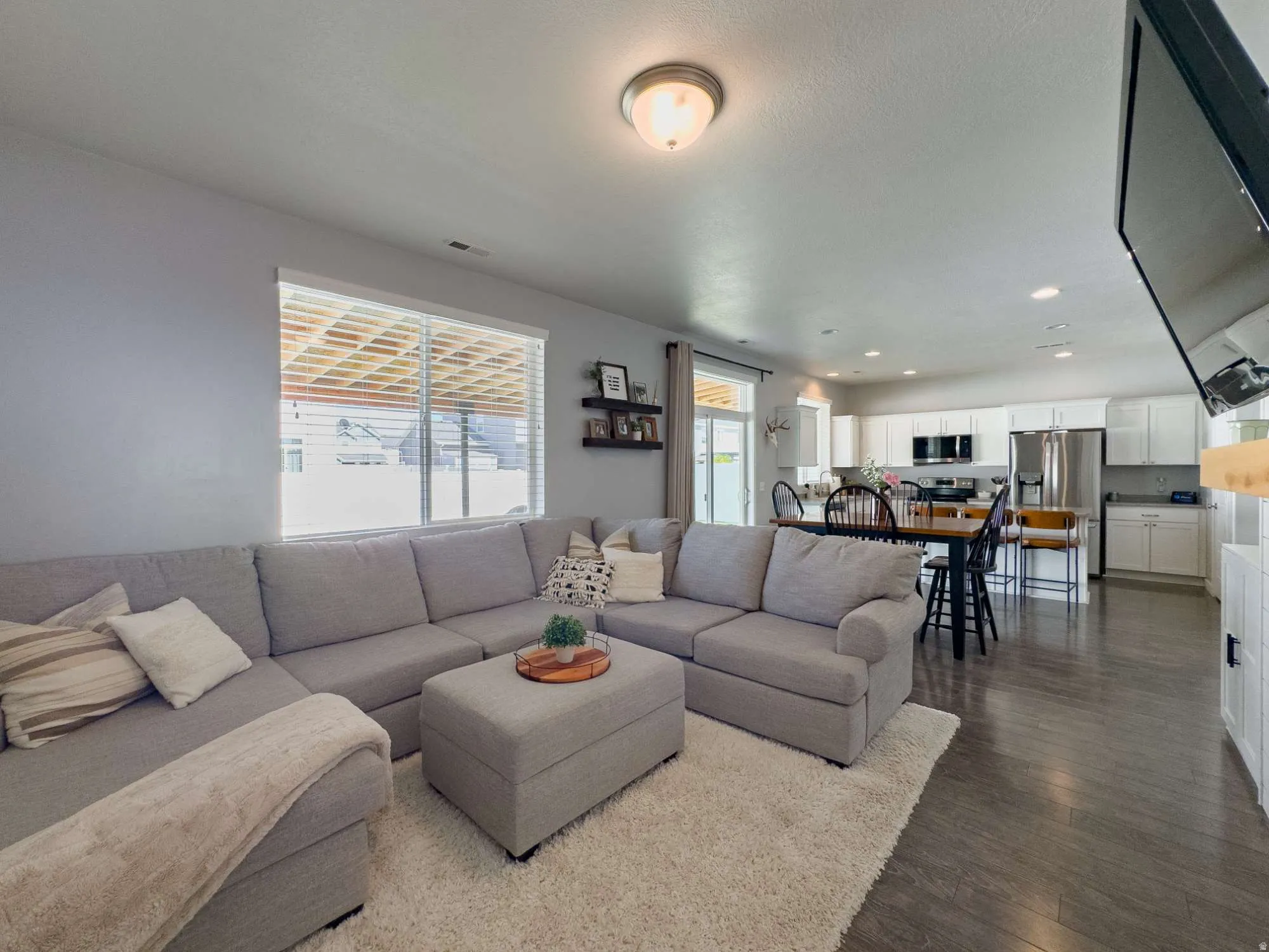 Open-concept living area featuring dark wood-finish flooring, recessed lighting, and a large window with horizontal blinds