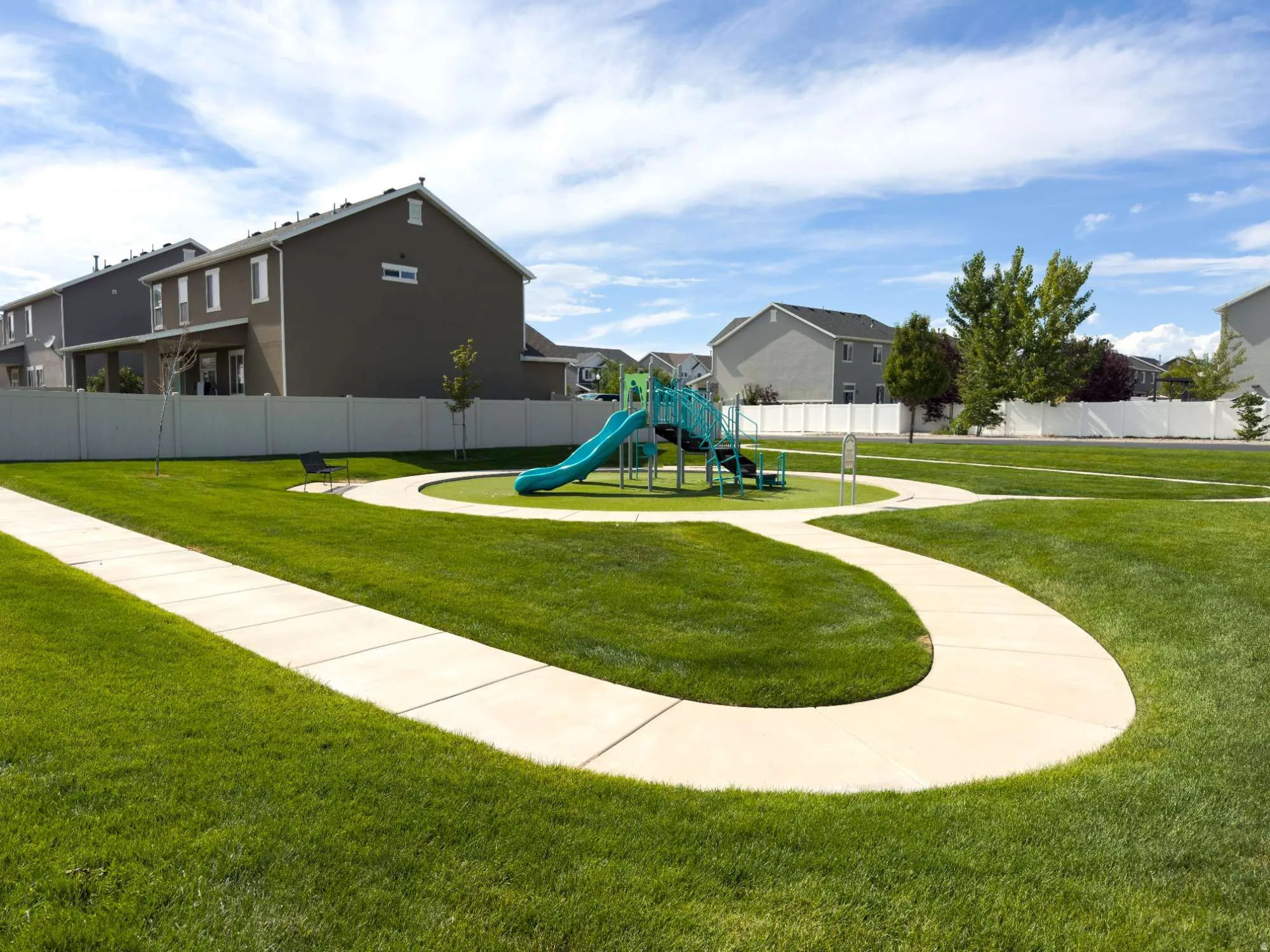 Green space featuring a playground with slides and climbing structures, surrounded by a white privacy fence