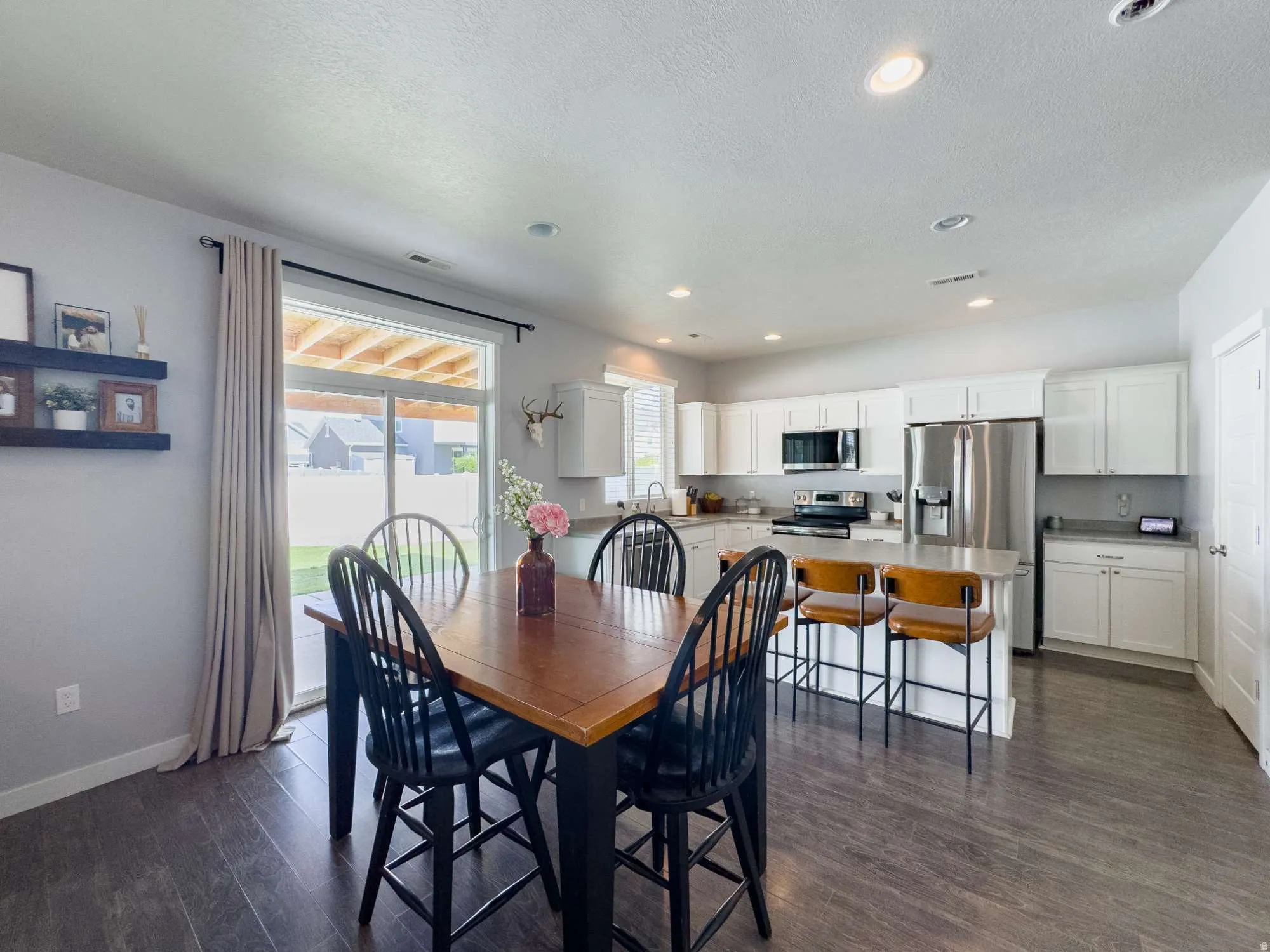 Open-concept dining and kitchen area featuring a wood-finish dining table with black Windsor-style chairs, stainless steel appliances, white cabinetry, and a center island with seating