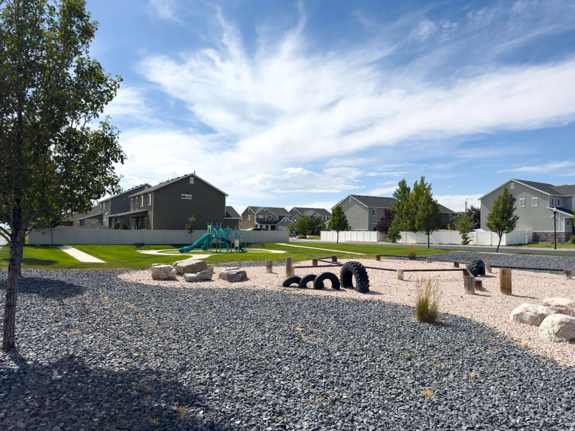 Expansive residential lot featuring a manicured lawn with mature trees, gravel hardscaping, and custom play structures