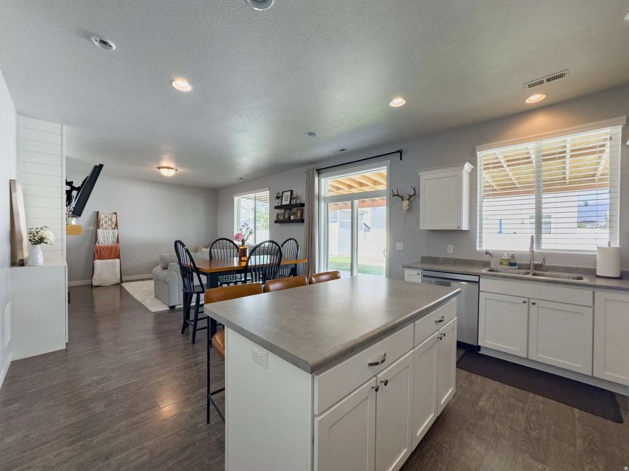 Modern open-concept kitchen and dining area featuring a large center island,  white cabinetry with hardware accents, stainless steel appliances, recessed and pendant lighting, wood-finish flooring throughout, and abundant natural light from multiple windo