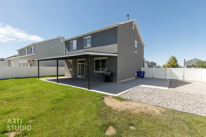 Expansive backyard featuring a manicured lawn, a large concrete patio with a covered section, and a white vinyl fence