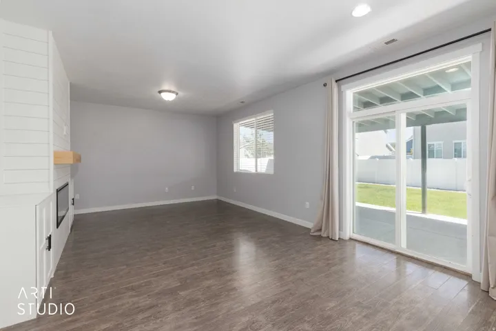 Living area featuring wood-finish flooring, a contemporary built-in fireplace with shiplap detailing and a wood mantel, and a sliding glass door leading to a concrete patio
