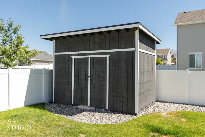 Detached, insulated storage shed with dark vertical siding, white trim, and a sloped roof