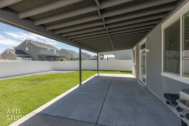 Covered patio with concrete flooring, stucco exterior, expansive lawn, and white privacy fencing