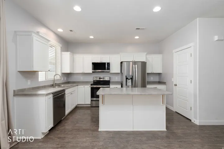 Kitchen featuring white cabinetry, light-toned countertops, stainless steel appliances, and wood-finish flooring