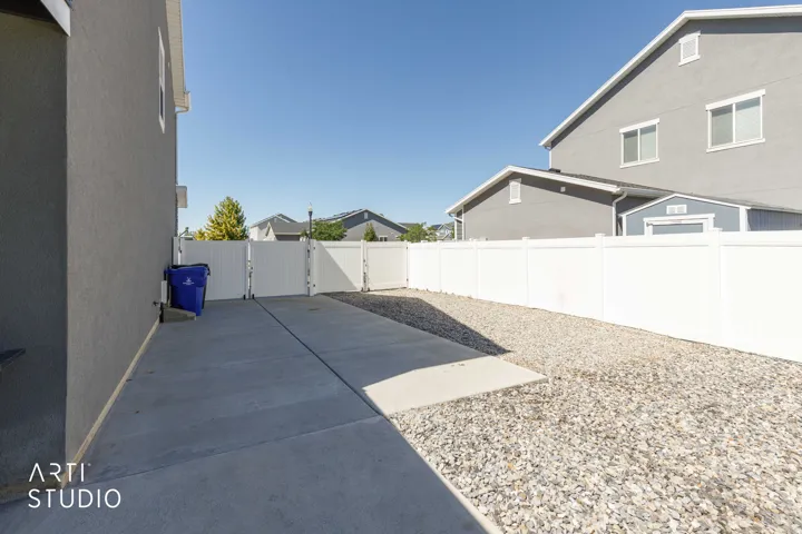 Paved RV pad extending to a gravel area, framed by a white privacy fence.