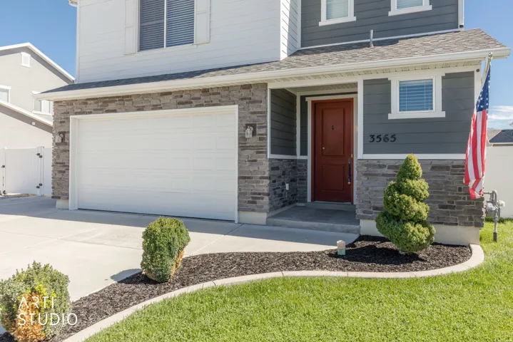 Two-story exterior with stone veneer accents, an attached garage, a covered entry, and a paved driveway