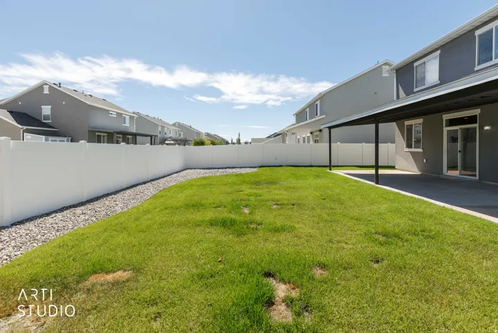 Spacious backyard featuring a covered patio, expansive lawn, white privacy fencing, and a gravel border