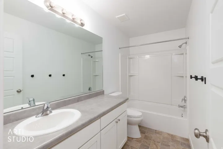 Bathroom featuring a single vanity with an integrated sink, white cabinetry, a full-width mirror, and a tub-shower combination with a white surround
