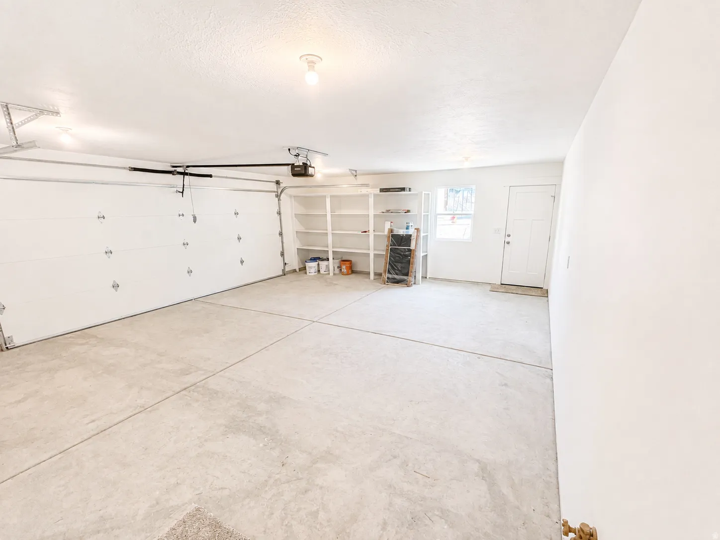 Spacious garage featuring a two-car overhead door with opener, concrete flooring, built-in shelving, and a side entry door with an opaque window